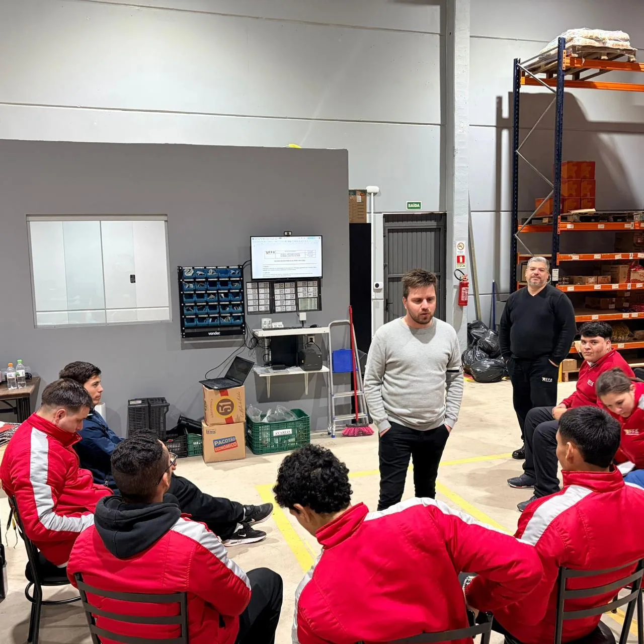 Treinamento prático conduzido dentro do armazém, com a equipe da operação em círculo.
